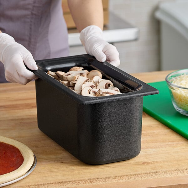 A person holding a Carlisle Coldmaster food pan filled with sliced mushrooms.