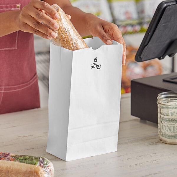 A woman putting a bag of bread in a Duro white paper bag.