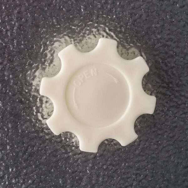 A white plastic gear-shaped freezer door knob with the word 'OPEN' and an arrow, mounted on a textured gray surface.