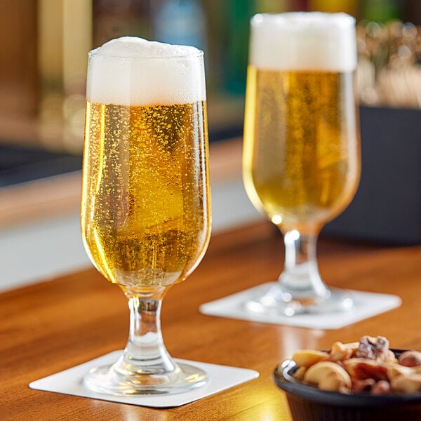 Two Libbey stemmed pilsner glasses filled with beer on a table.