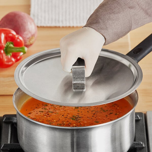 A person wearing gloves is holding a Vollrath Tribute pan cover over a pot of soup.