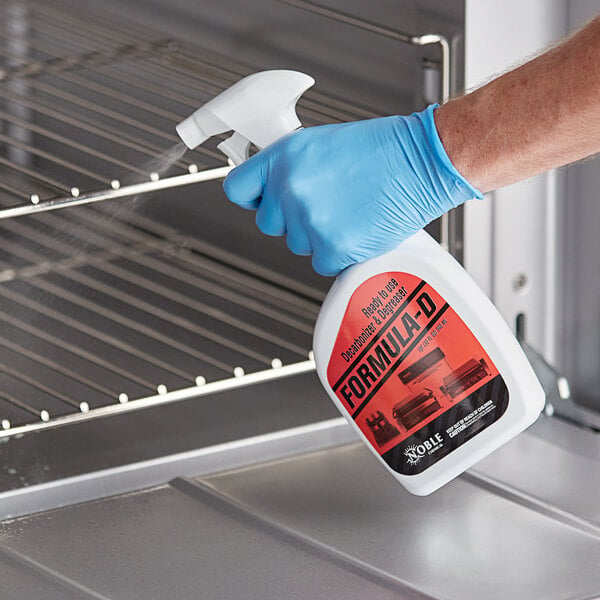 A person wearing blue gloves spraying Noble Chemical Formula-D degreaser on an oven.