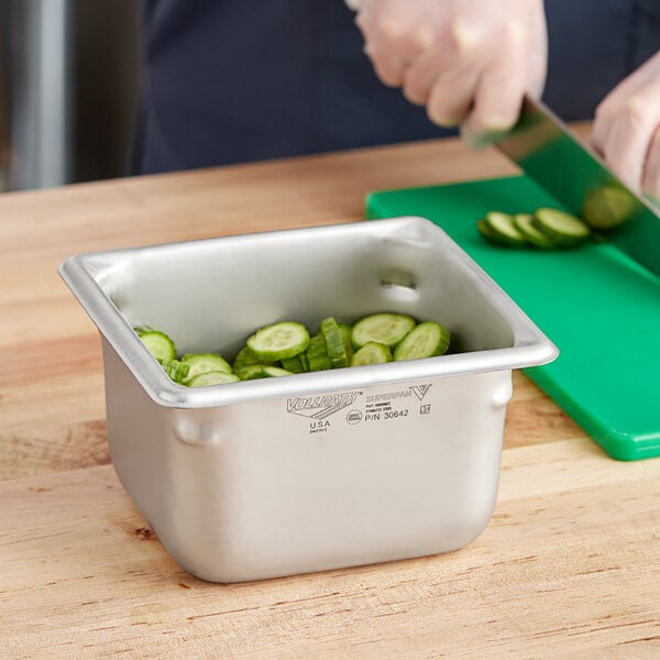 A person cutting cucumbers in a Vollrath stainless steel hotel pan.