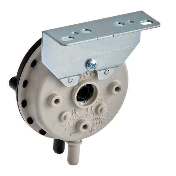 A round, beige plastic component with two protruding nozzles and a metal mounting bracket attached to the top.