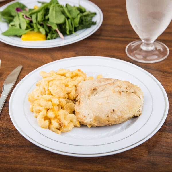 A Fineline white plastic plate with silver bands filled with chicken and macaroni on a table.