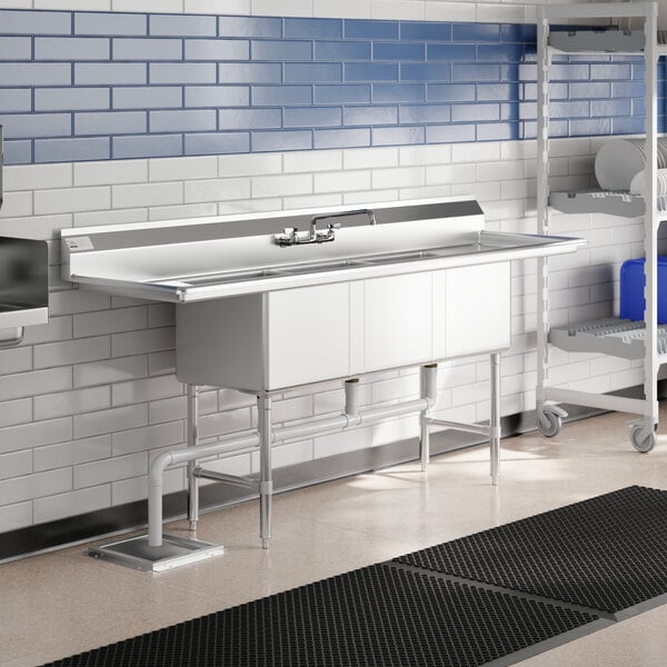 A stainless steel Advance Tabco three compartment sink with two drainboards over a sink with a faucet.