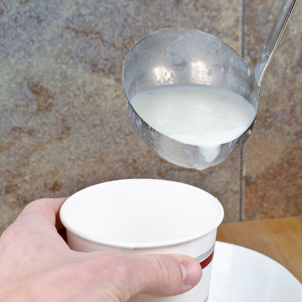 A hand using a Vollrath stainless steel ladle to pour white liquid into a cup.
