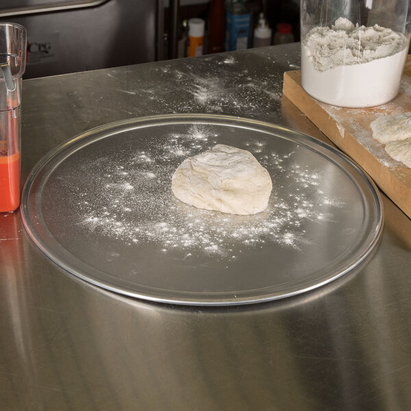 A dough ball on an American Metalcraft aluminum pizza pan on a counter.