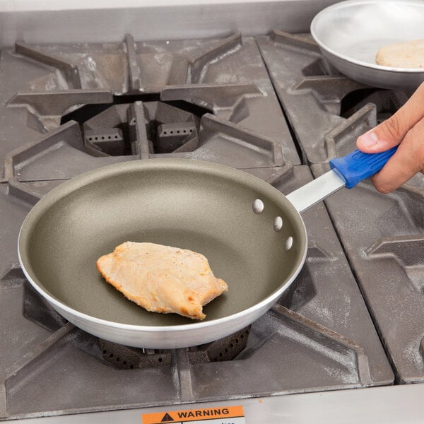 A person frying chicken in a Vollrath aluminum non-stick fry pan with a blue handle.