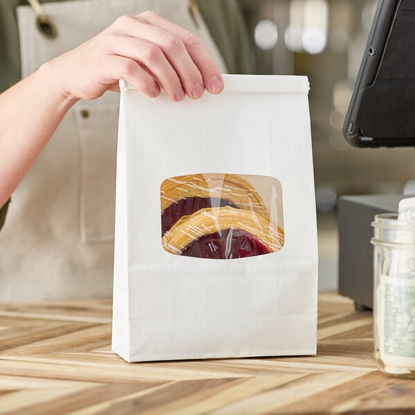 A person holding a white Choice paper bag with a clear plastic window filled with food.