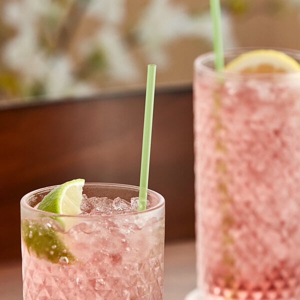 Two glasses of pink drink with lime slices and green unwrapped Collins straws.