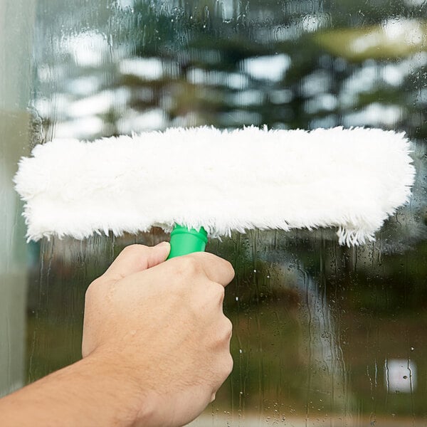 A hand using a green Unger StripWasher sleeve to clean a window.