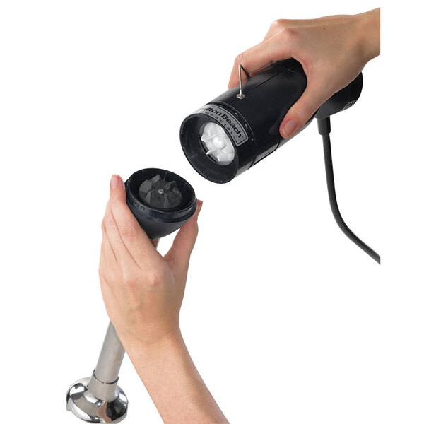 A hand holding a black Hamilton Beach chopping attachment for an immersion mixer.