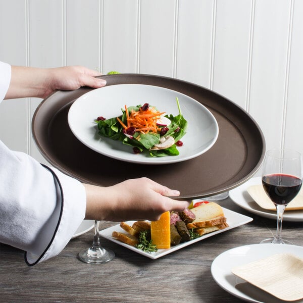 A chef holding a Cambro Tavern Tan non-skid serving tray with a plate of food.