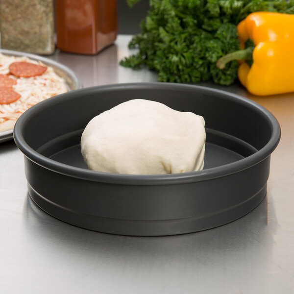 A white round ball of pizza dough in a black pan.