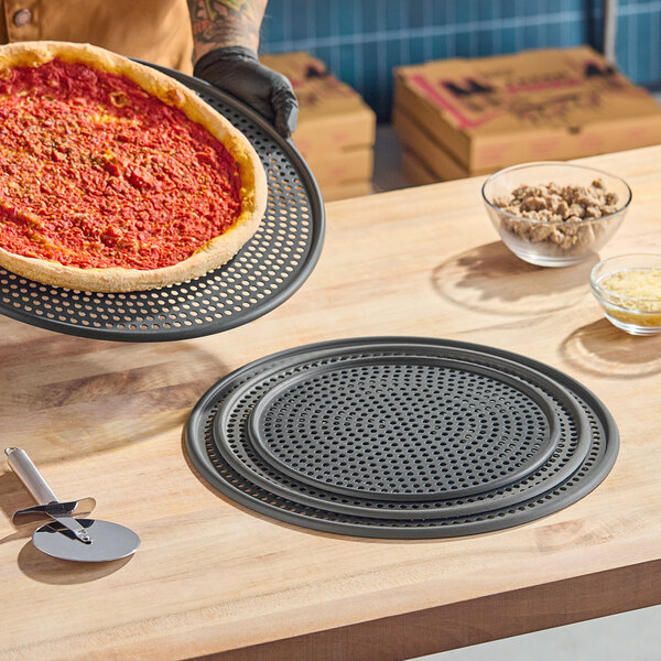 A round, perforated hard coat anodized aluminum pizza screen on a wooden countertop.