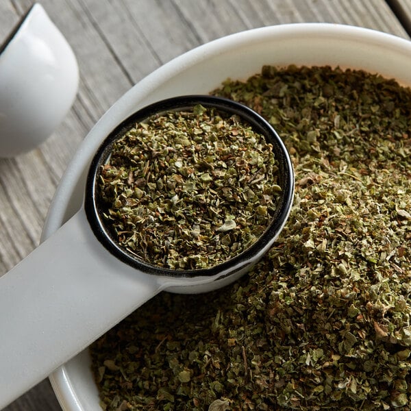 Scooping dried marjoram leaves out of a bowl with a measuring spoon