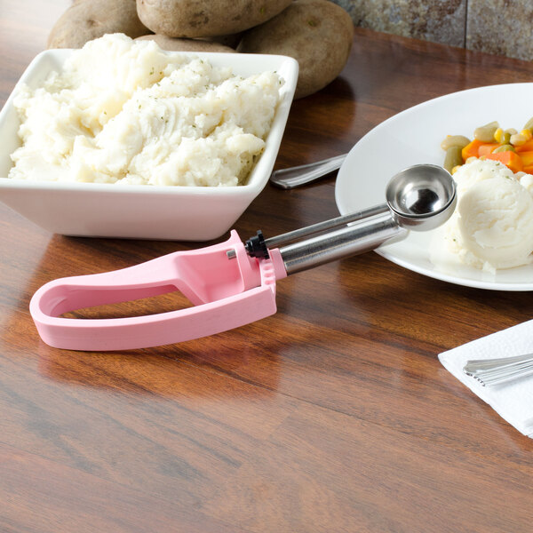 A plate of mashed potatoes with a Vollrath pink and silver extended length squeeze handle disher on the table.