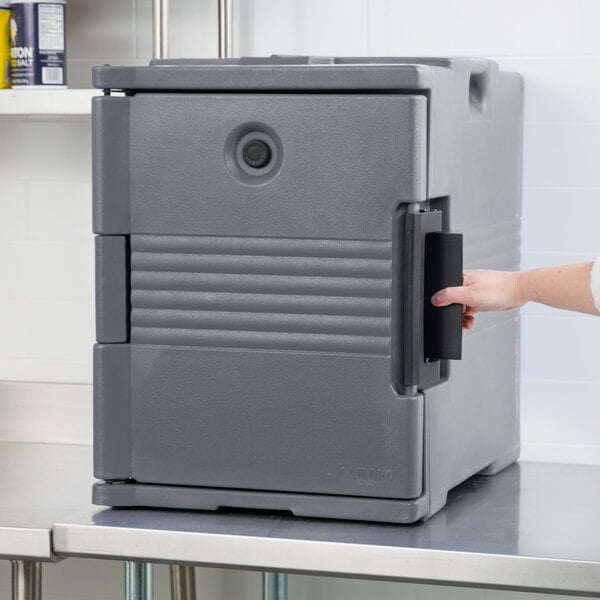 A hand opening a grey Cambro Ultra Pan Carrier on a counter.