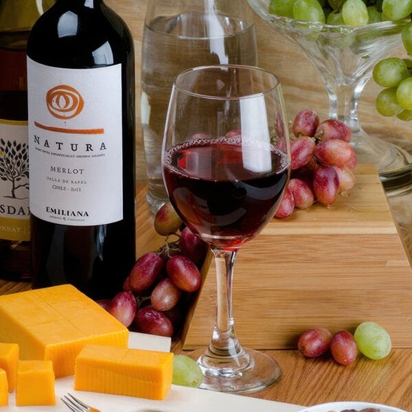 A Libbey tall wine glass filled with red wine next to a bowl of grapes.