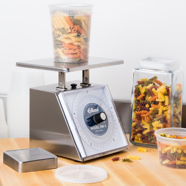 An Edlund portion scale on a counter weighing a plastic container of pasta.