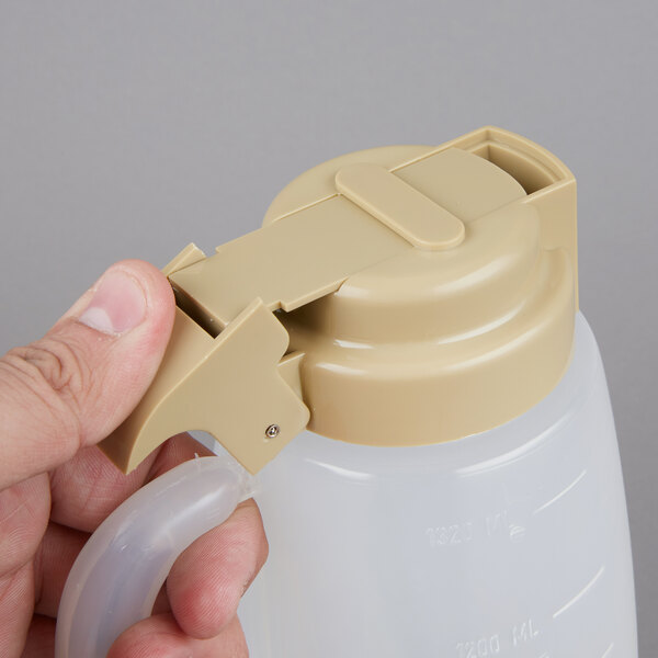 A person holding a Tablecraft 48 oz. plastic dispenser with a beige top.