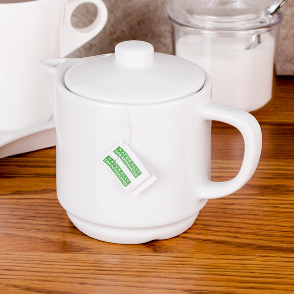 An Arcoroc white porcelain teapot with a tea bag on it.
