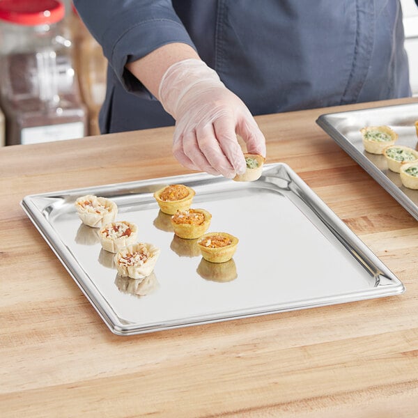 A person putting food on a Vollrath stainless steel tray.