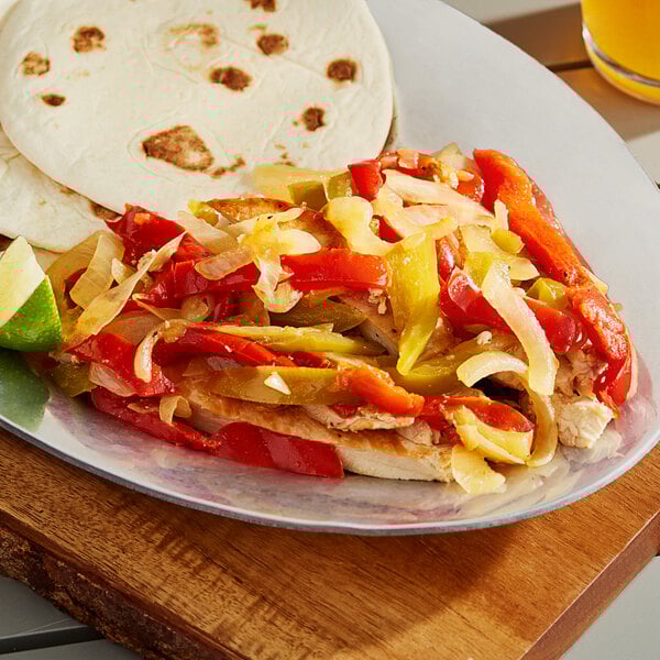 A plate of tortillas, chicken, and mixed pepper strips with onions on a table.