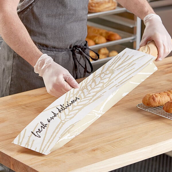 A person holding a paper bag with a loaf of bread inside.