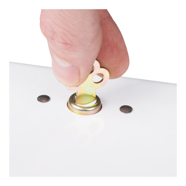 A close-up of a hand operating the lock mechanism on a white paper towel dispenser.