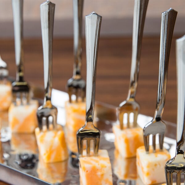 A tray of WNA Comet Reflections Petites stainless steel look plastic tasting forks on a table with food.