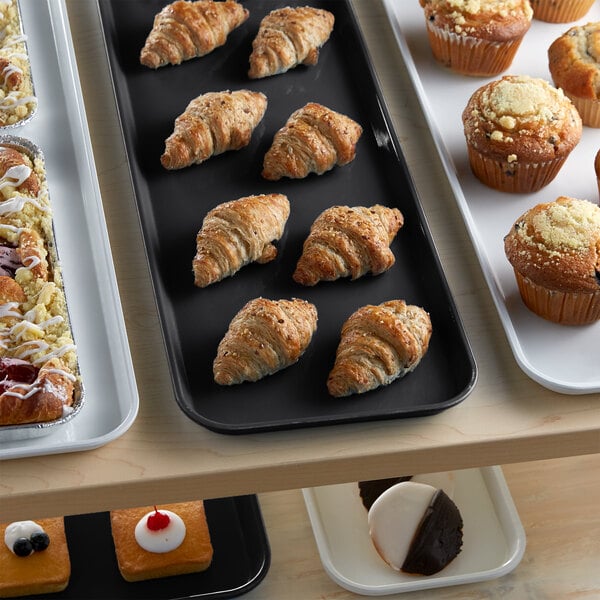 A black Cambro market tray holding pastries and muffins on a bakery display counter.