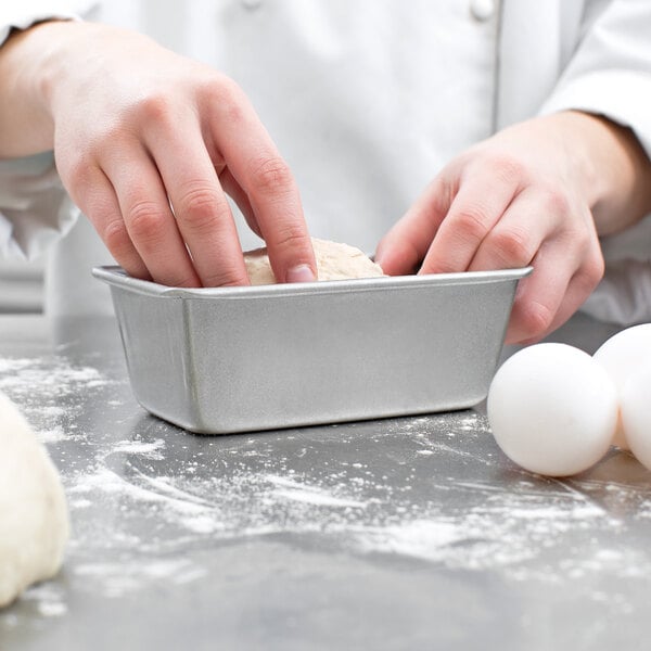 A person's fingers holding dough in a Chicago Metallic bread loaf pan.