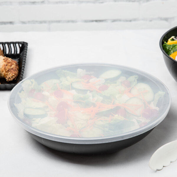 A black Fineline disposable plastic bowl filled with salad on a table.