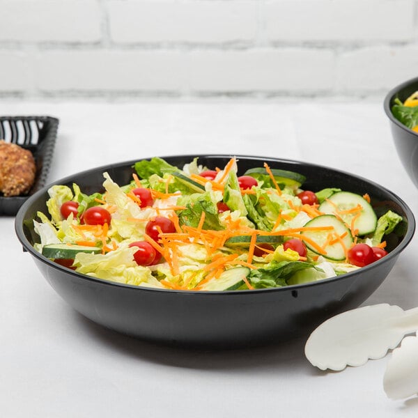 A bowl of salad with tomatoes, carrots, and a fork in a Fineline black plastic bowl.