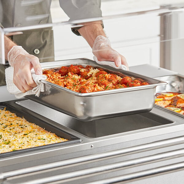 A person holding a Vollrath stainless steel steam table pan with food on a tray.