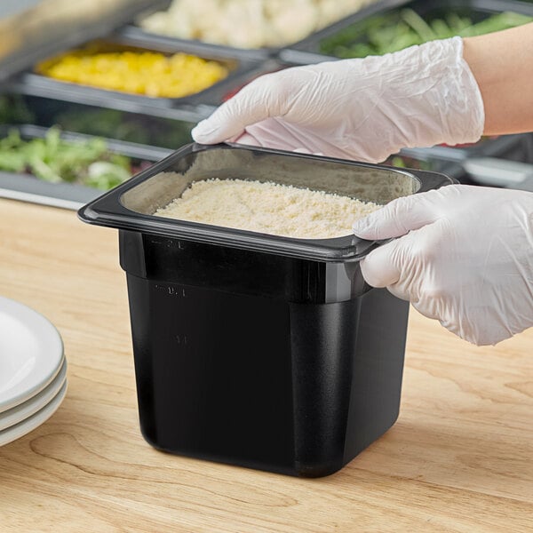 A person in gloves holding a black Cambro food container on a counter.