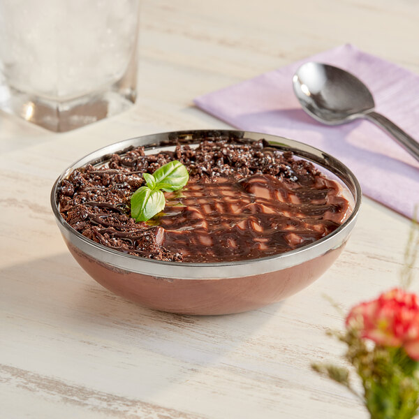 A Sabert clear plastic bowl filled with chocolate pudding with a spoon on a napkin.