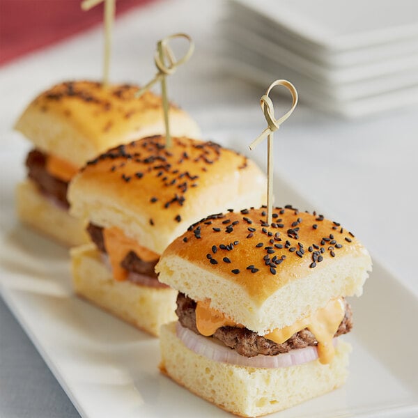 Three mini burgers on a white plate with Royal Paper Eco-Friendly Knot Bamboo Food Picks.