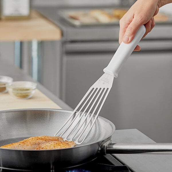 A hand using a Victorinox slotted spatula to cook food in a pan.