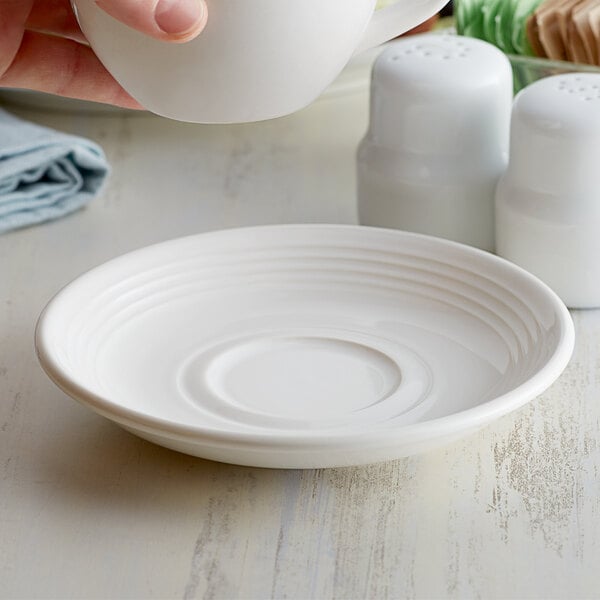 A person's hand holding a white Tuxton saucer and cup.