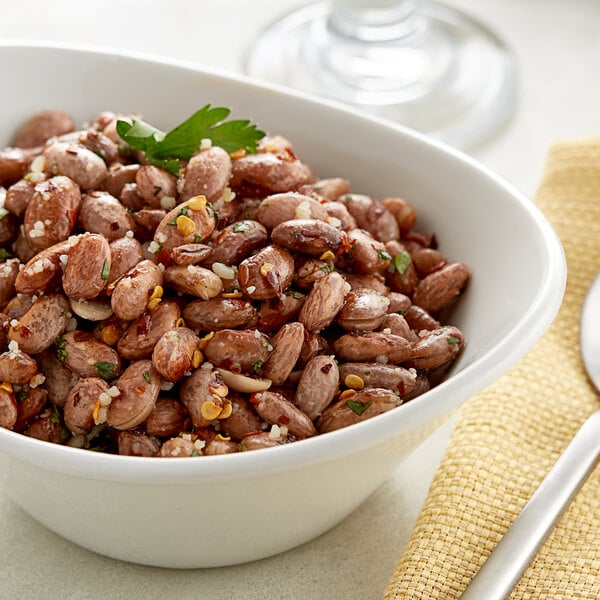 A white bowl of dried pinto beans with parsley and a spoon.