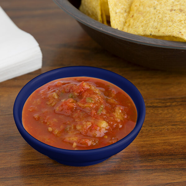 A cobalt blue melamine salsa dish filled with salsa on a table with a bowl of chips.