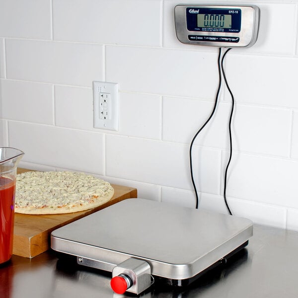 A stainless steel Edlund digital pizza scale on a kitchen counter with a pizza.