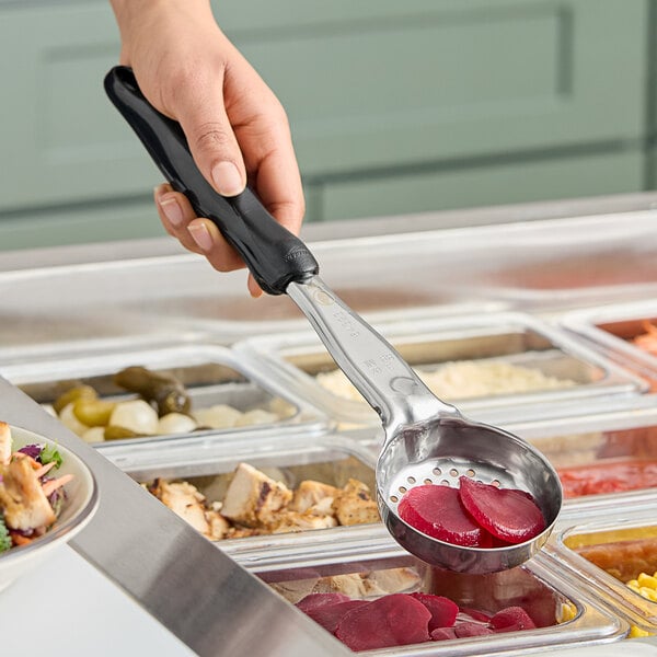 A hand holding a Vollrath black perforated round Spoodle over a bowl of food.
