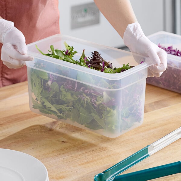 A gloved hand uses a Cambro translucent plastic food pan to serve green salad leaves.