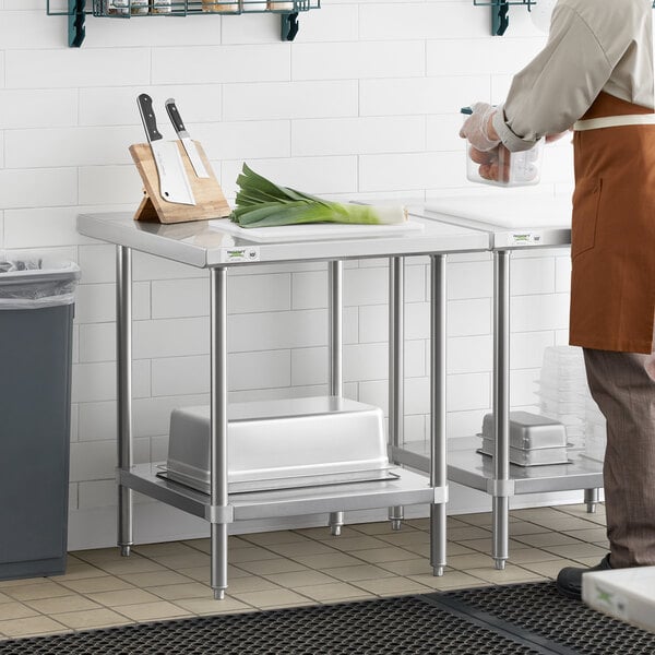 A man in an apron standing next to a Regency stainless steel work table with undershelf in a professional kitchen.