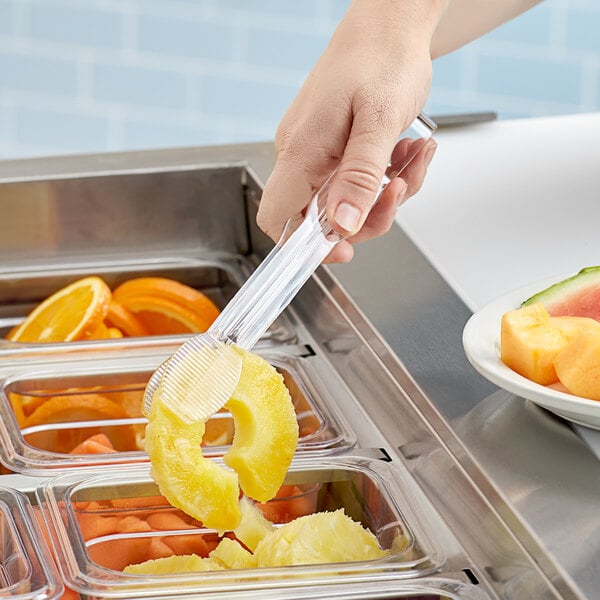 A hand using Cambro flat grip plastic tongs to serve fruit from a salad bar.