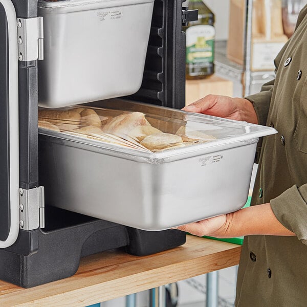 A person holding a Vollrath stainless steel container of food.